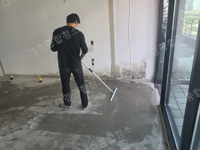 밀대로 젖은 바닥 물기를 밀어내는 검은 옷 작업자