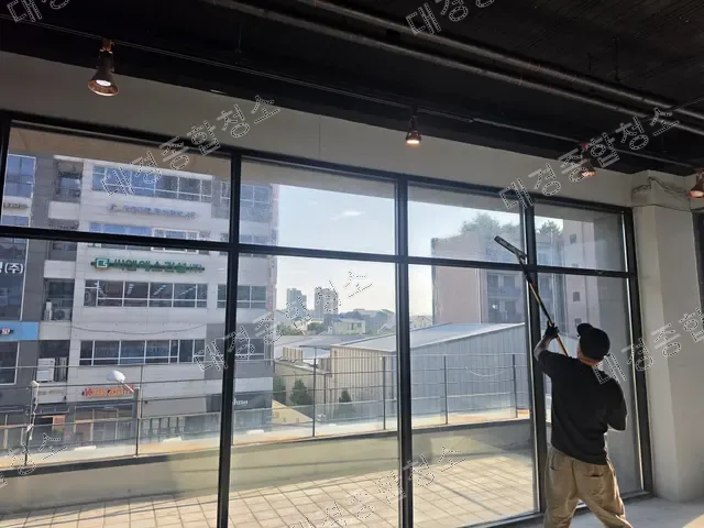 T바로 대형 유리창 안쪽을 닦는 작업자와 도심 전경