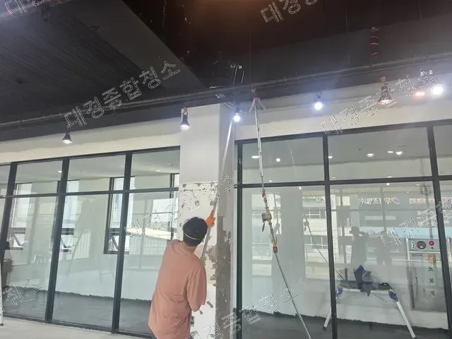 실내 기둥 표면을 정리하는 작업자와 통유리창