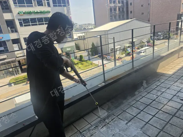 난간 옆 테라스 타일 바닥을 고압세척하는 작업자