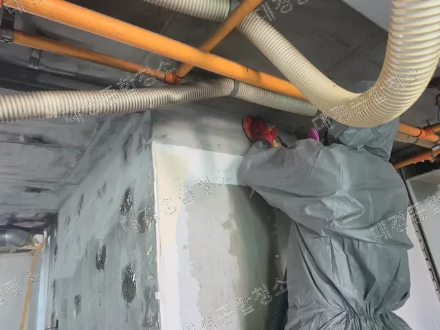 벽면 상단 모서리를 샌딩하는 방진복 작업자